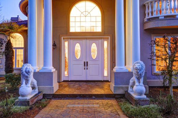Mediterranean style luxury waterfront home boasts elegant high ceiling porch with white columns and lion statues leading to front door with arch window and sidelights, sunset view. Northwest, USA