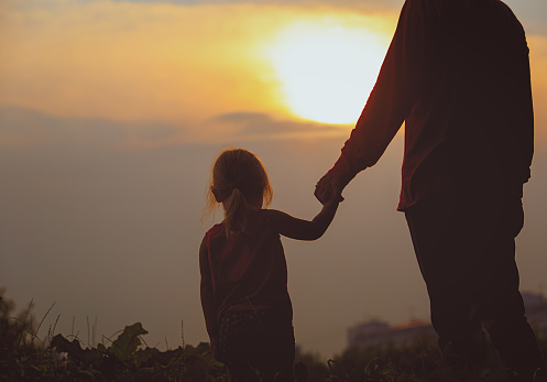 silhouette of father and daughter holding hands at sunset sky