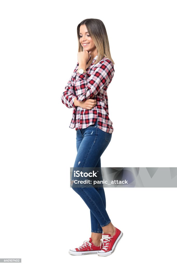 Gorgeous street style woman wearing jeans, plaid shirt and sneakers Gorgeous street style woman wearing jeans, plaid shirt and sneakers smiling looking down. Full body length portrait isolated over white studio background. Women Stock Photo