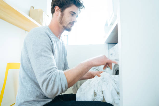 Man At Home Doing Laundry Man at home doing laundry, putting clothes in the washing machine. laundry husband housework men stock pictures, royalty-free photos & images