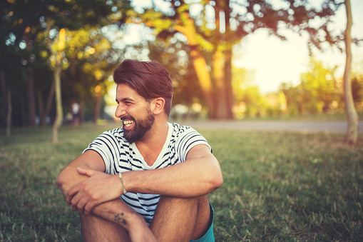Portrait of laughing man in the park,sitting on the grass in summer,day