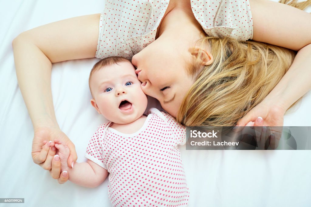 Mother kisses baby lying on the bed closeup Mother kisses baby lying on the bed closeup. Mother Stock Photo