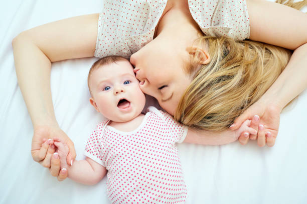 mother kisses baby lying on the bed closeup - mother baby new kissing imagens e fotografias de stock