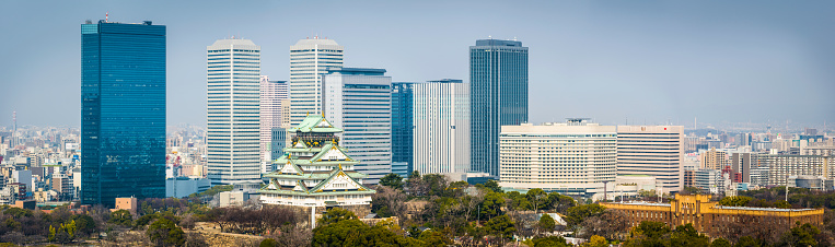 Osaka, Japan - February 28, 2016: The iconic five storey tower of Osaka Castle surrounded by the leafy foliage of Osaka Castle Park and overlooked by the modern skyscrapers of downtown Osaka, Japan's vibrant second city. Panoramic image created from ten contemporaneous sequential photographs. 