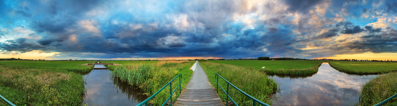 Beautiful vibrant 360 degree panorama of a polder landscape in the Netherlands with a typical dutch cloudy sky in spring