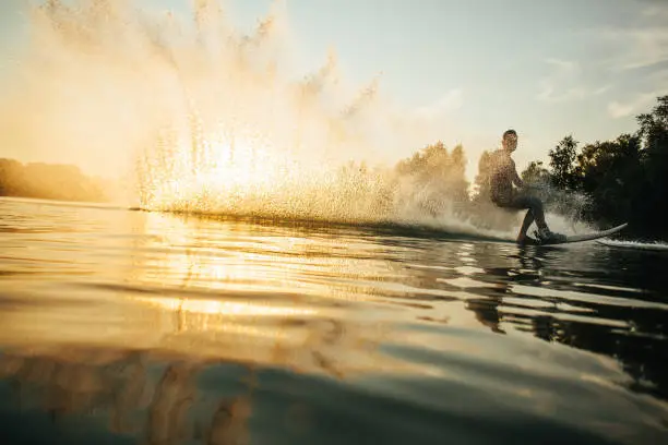 Low angle shot of man wakeboarding on a lake. Man water skiing at sunset.