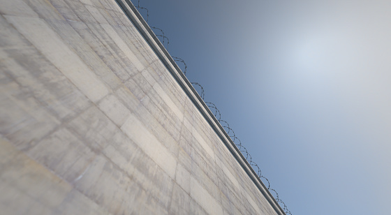A 3D render of a massively high concrete security wall topped with barbed wire on a blue sky background