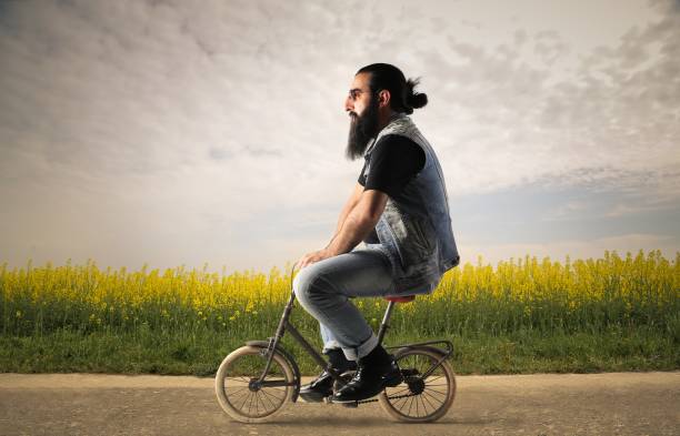 Small bicycle for a big boy Bearded man is sitting on a small bicycle cycle vehicle photos stock pictures, royalty-free photos & images