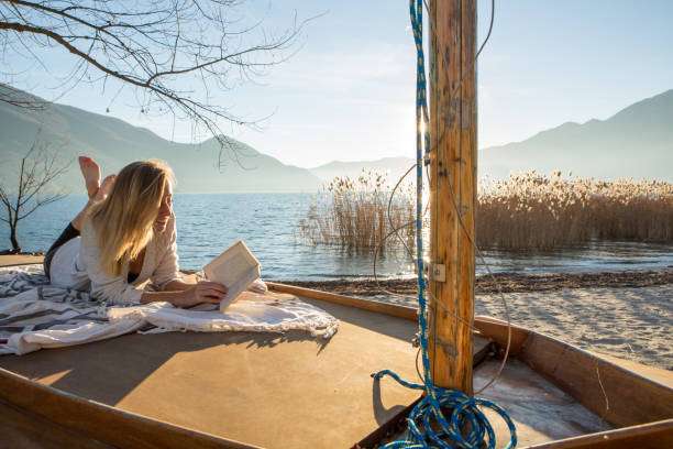 istock Young woman relaxing by the lake reading book 640154694