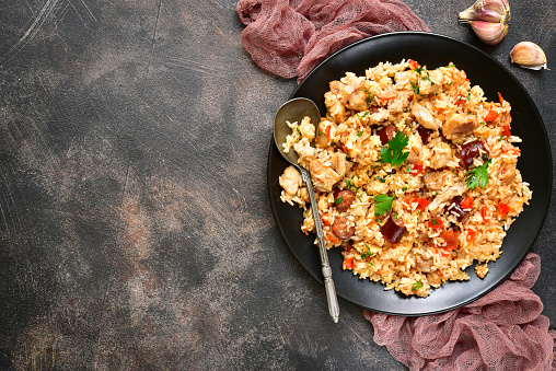 Jambalaya - spicy rice with meat and vegetables on a black plate on a dark rustic metal,slate or stone background.Top view.