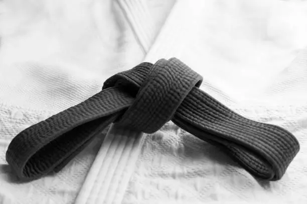 Black judo, aikido or karate belt tied in a knot with white kimono in background