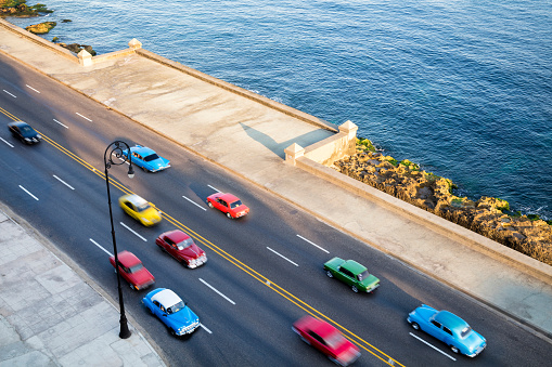 Vintage American cars speeding along the Malecon in Havana, Cuba, motion blur, Caribbean Sea is visible in the background, elevated view, 50 megapixel image.