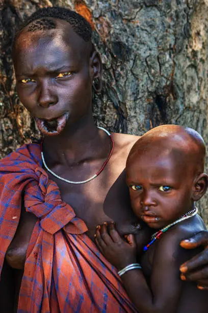 Woman from Mursi tribe breasfeeding her baby.  Mursi tribe are probably the last groups in Africa amongst whom it is still the norm for women to wear large pottery or wooden discs or ‘plates’ in their lower lips.http://bhphoto.pl/IS/ethiopia_380.jpg