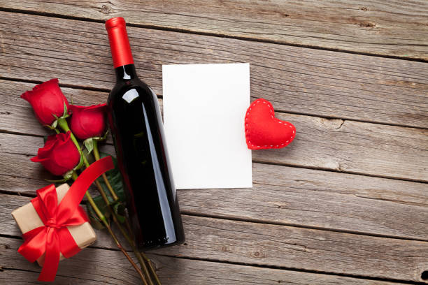 Valentines day greeting card Valentines day greeting card. Red wine, roses and gift box on wooden table. Top view with copy space rose bouquet red table stock pictures, royalty-free photos & images