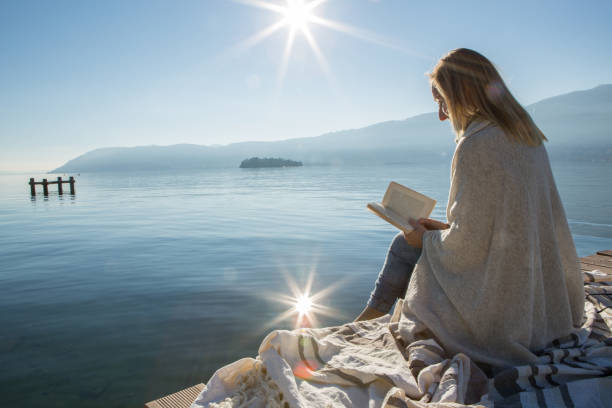 istock Young woman relaxing on lake pier with book 640189574