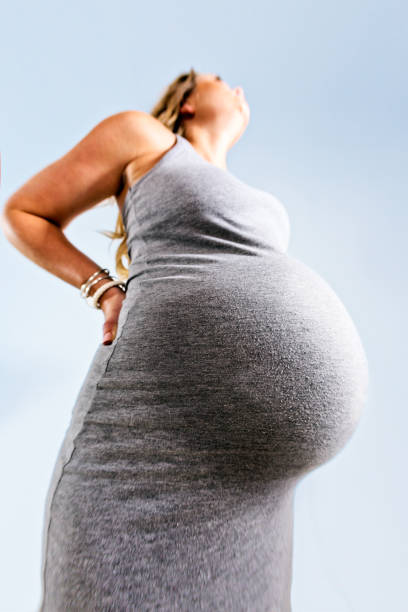 Low-angle look at very pregnant woman's distended tummy Looking up with exaggerated perspective at an extremely pregnant woman's bulging belly - the baby is nearly due. full term stock pictures, royalty-free photos & images