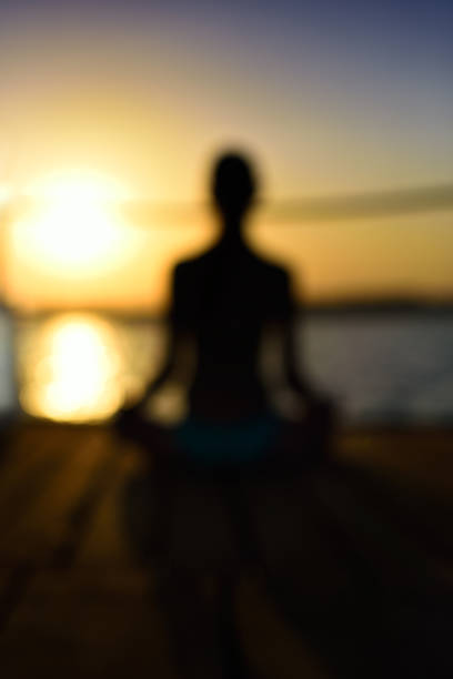 blurred image back woman sitting in a lotus pose on the wooden planks, sunset, vertical