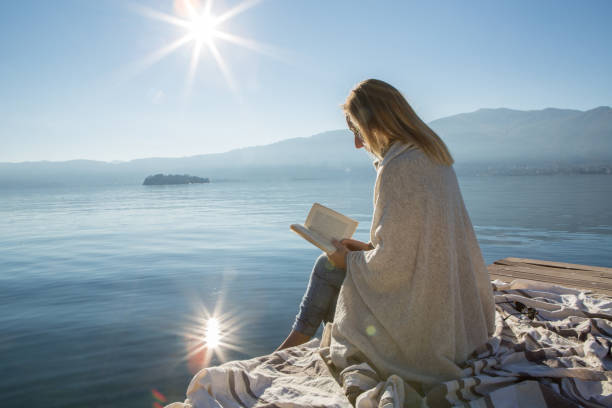 istock Young woman relaxing on lake pier with book 640199012