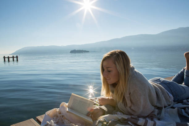 istock One young woman lying down on lake pier, reading book 640199080
