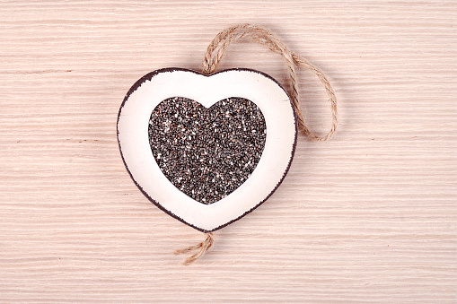 White heart shaped frame filled with chia seeds, on white oak wood.