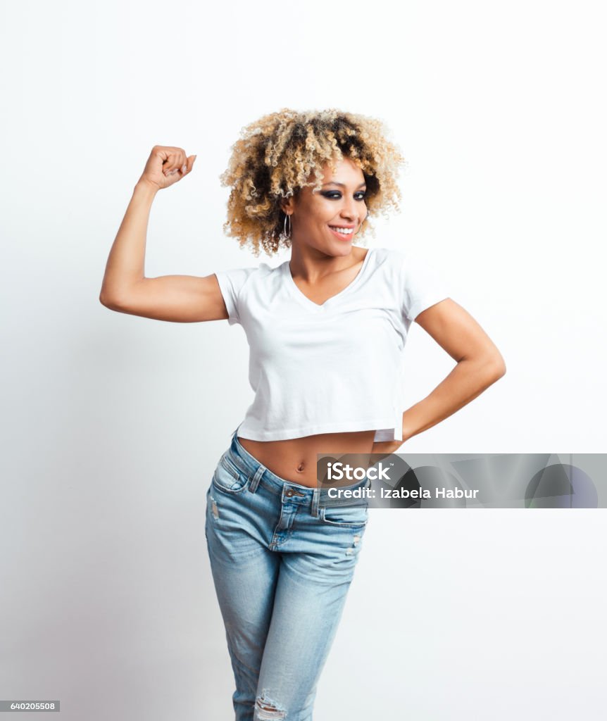 Confident afro american young woman Confident afro american young woman flexing her arm, smiling at camera. Studio shot, white background. Adult Stock Photo