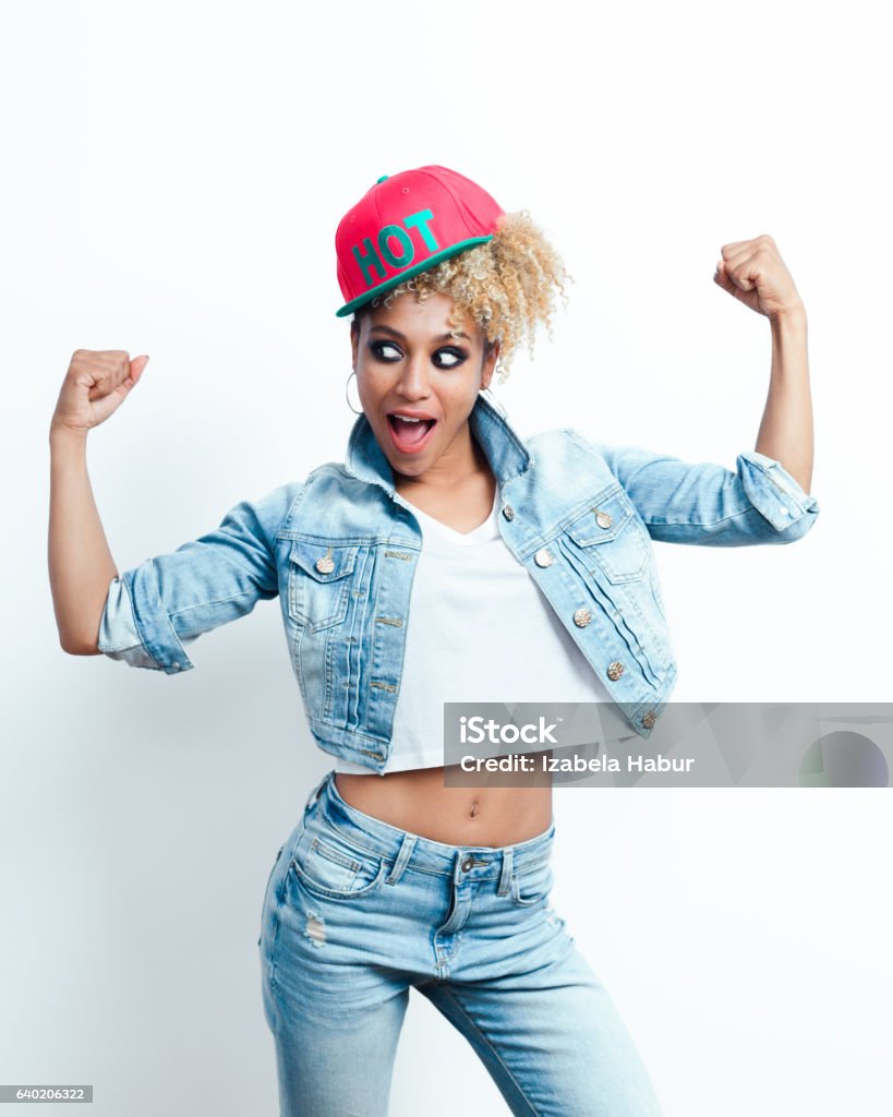 Successful afro american young woman Successful afro american young woman wearing denim jacket and baseball cap, flexing her arms and shouting. Studio shot, white background. Adult Stock Photo