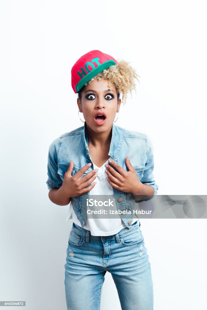 Shocked afro american young woman Shocked afro american young woman wearing denim jacket and baseball cap, staring at the camera with mouth open. Studio shot, white background. African-American Ethnicity Stock Photo