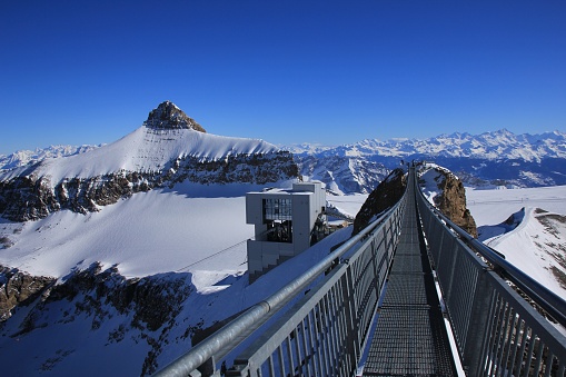 Winter scene on the Glacier de Diablerets. Mount Oldenhorn. Suspension bridge connecting two mountain peaks. Summit station of a cable car.