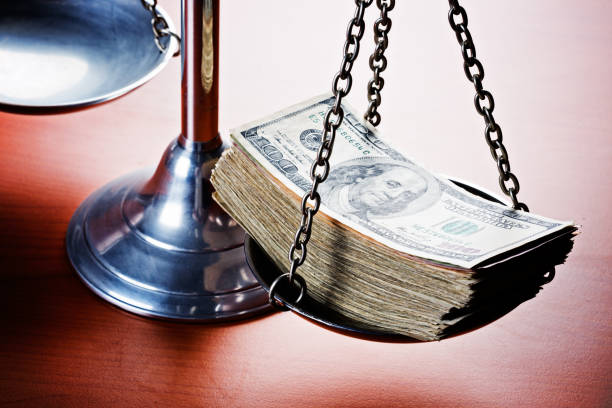 The symbolic Scales of Justice here have a fat stack of American Hundred Dollar banknotes on one side signifying a massive bribe and corruption in the legal system.