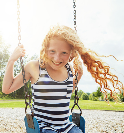 Portrait of a young girl playing on a swing at the park
