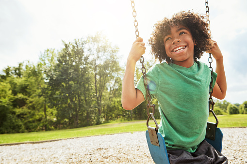 Cropped shot of a young boy playing on a swing at the park