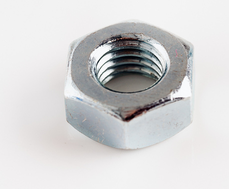 One brightly lit and shiny stainless steel nut on a white background with copy space.