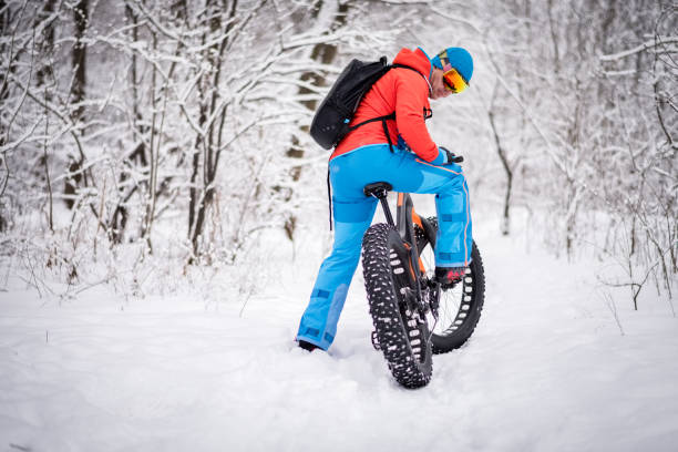 Male cyclist with backpack and ski goggles riding his fat bike on a winter day somewhere in the woods. Area is covered with snow.