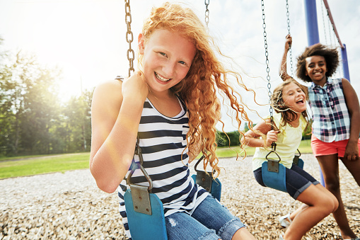 Portrait of a young girl playing on a swing at the park with her friends
