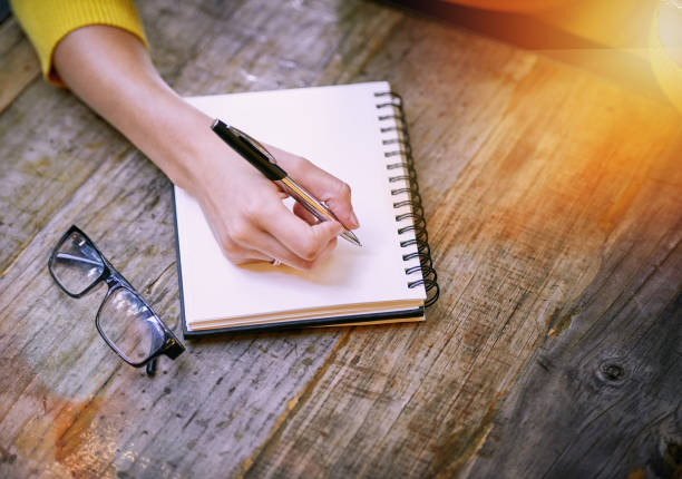 Cropped shot of a woman sitting at a table and writing in her notepad
