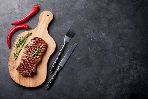 Grilled beef steak on cutting board over stone table. Top view with copy space