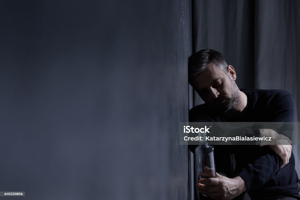 Man holding bottle of alcohol Man holding bottle of alcohol in dark interior Detox Stock Photo