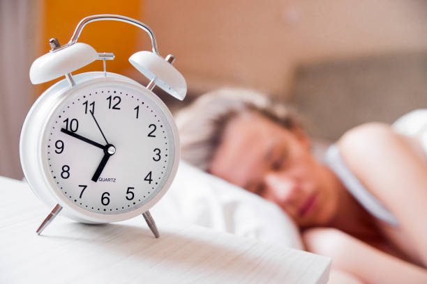 istock Alarm clock on table and woman sleeping in background 640221128