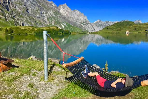 A young boy is lying in a hammock at Trübsee mountain lake in Engelberg Switzerland on a beautiful summer day.