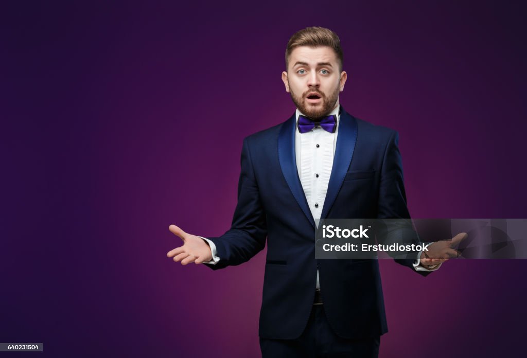 Handsome man in tuxedo and bow tie is surprised, throws Handsome man in tuxedo and bow tie is surprised and throws his hands. compere in fashionable, festive clothing on dark background Men Stock Photo