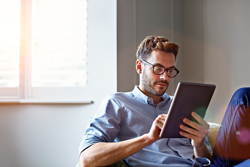 Shot of a young man sitting on his sofa at home using a digital tablet