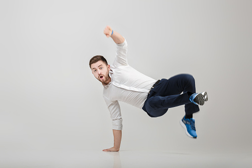 young happy businessman with beard in white shirt break dancing on grey background