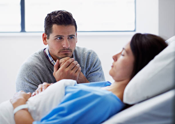 Please get better... Shot of an unconscious woman lying in a hospital bed being comforted by her husband nervous holding hands stock pictures, royalty-free photos & images