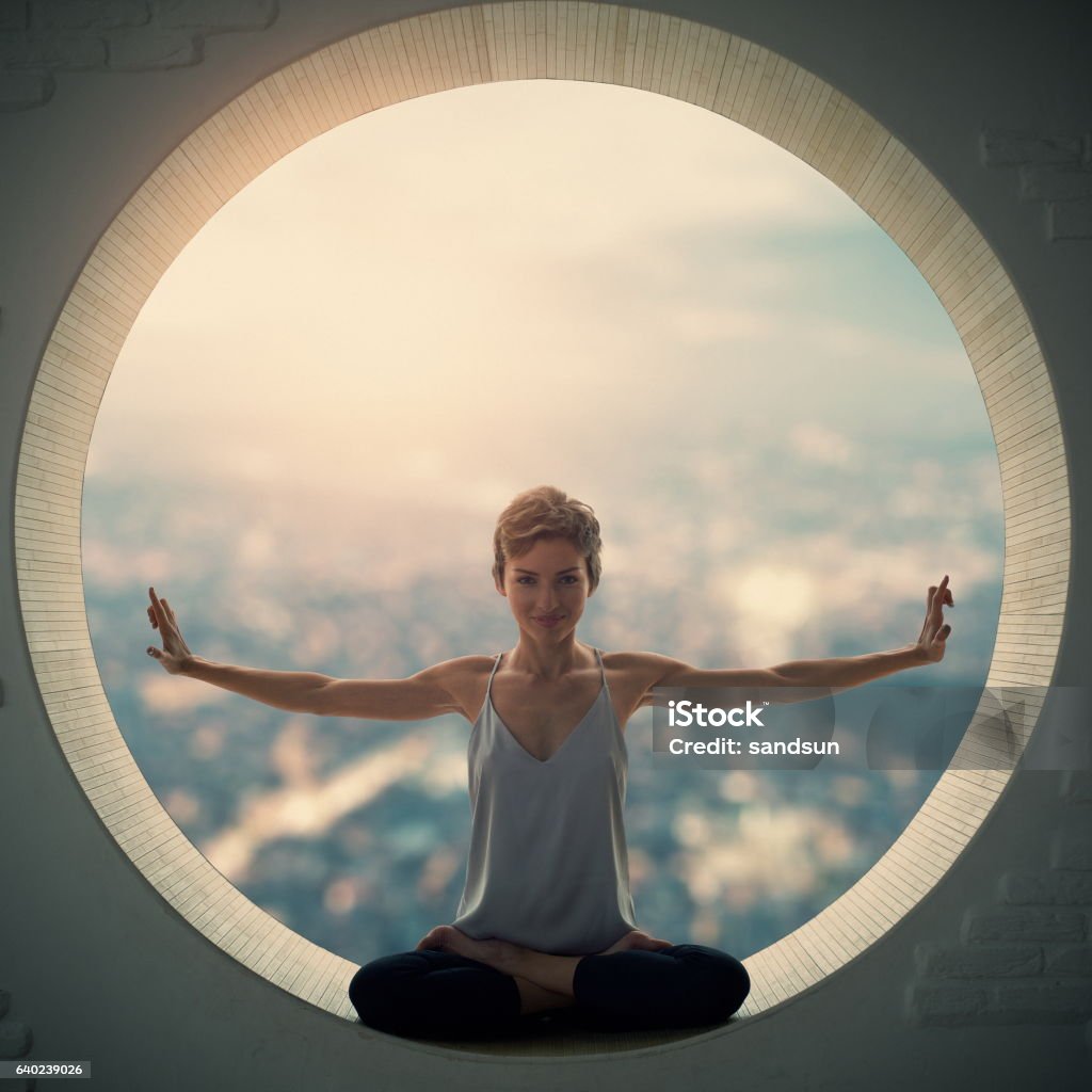 young woman sitting in lotus posture young woman doing yoga in the round window Circle Stock Photo