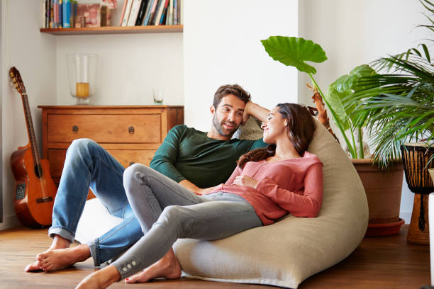 Spending the day chilling together Shot of a smiling young couple talking together while relaxing on a beanbag sofa at home Love stock pictures, royalty-free photos & images