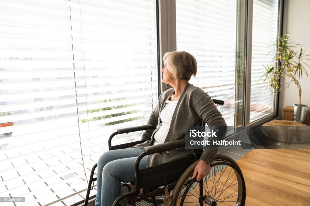 Mujer mayor discapacitada en silla de ruedas en casa en la sala de estar. - Foto de stock de Silla de ruedas libre de derechos