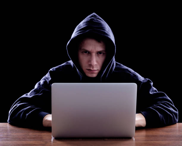 istock Hacker in dark hoody sitting in front of notebook 640242598