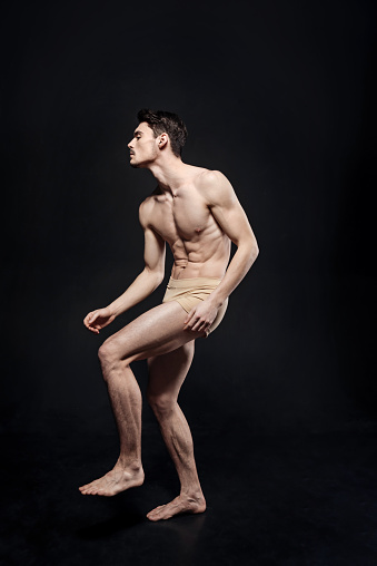 Expressing my personality. Skilled muscular young ballet dancer demonstrating his abilities and expressing creativity while standing against black background