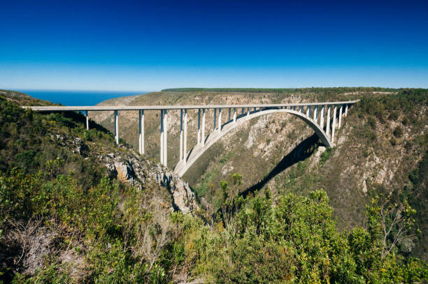 Vehicles driving on a large bridge running over a ravine in scenic lush hilly countryside on an overcast day
