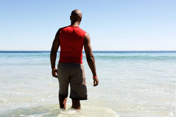 homme africain marchant dans l’eau de mer - shorts rear view summer beach photos et images de collection